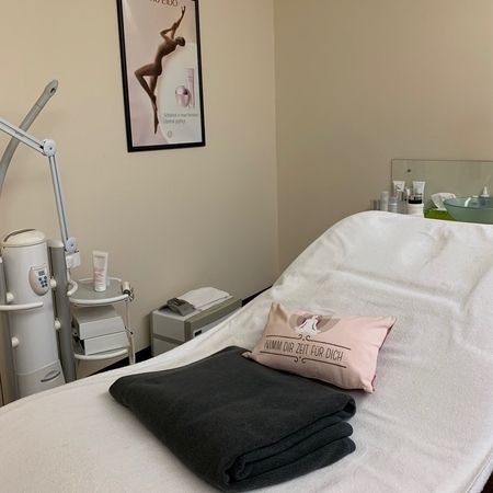 Ein Spa-Behandlungsraum mit einer Massageliege mit Decken, einem dekorativen Kissen und Hautpflegeprodukten