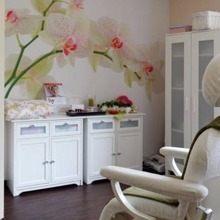 Ein ruhiger Wellness-Raum mit einem weißen Behandlungsstuhl, einem Schrank und einem Wandbild mit Orchideen
