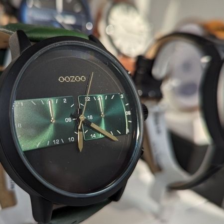 Eine stilvolle Uhr mit grünem Zifferblatt und schwarzem Gehäuse, mit goldenen Zeigern und grünem Lederarmband