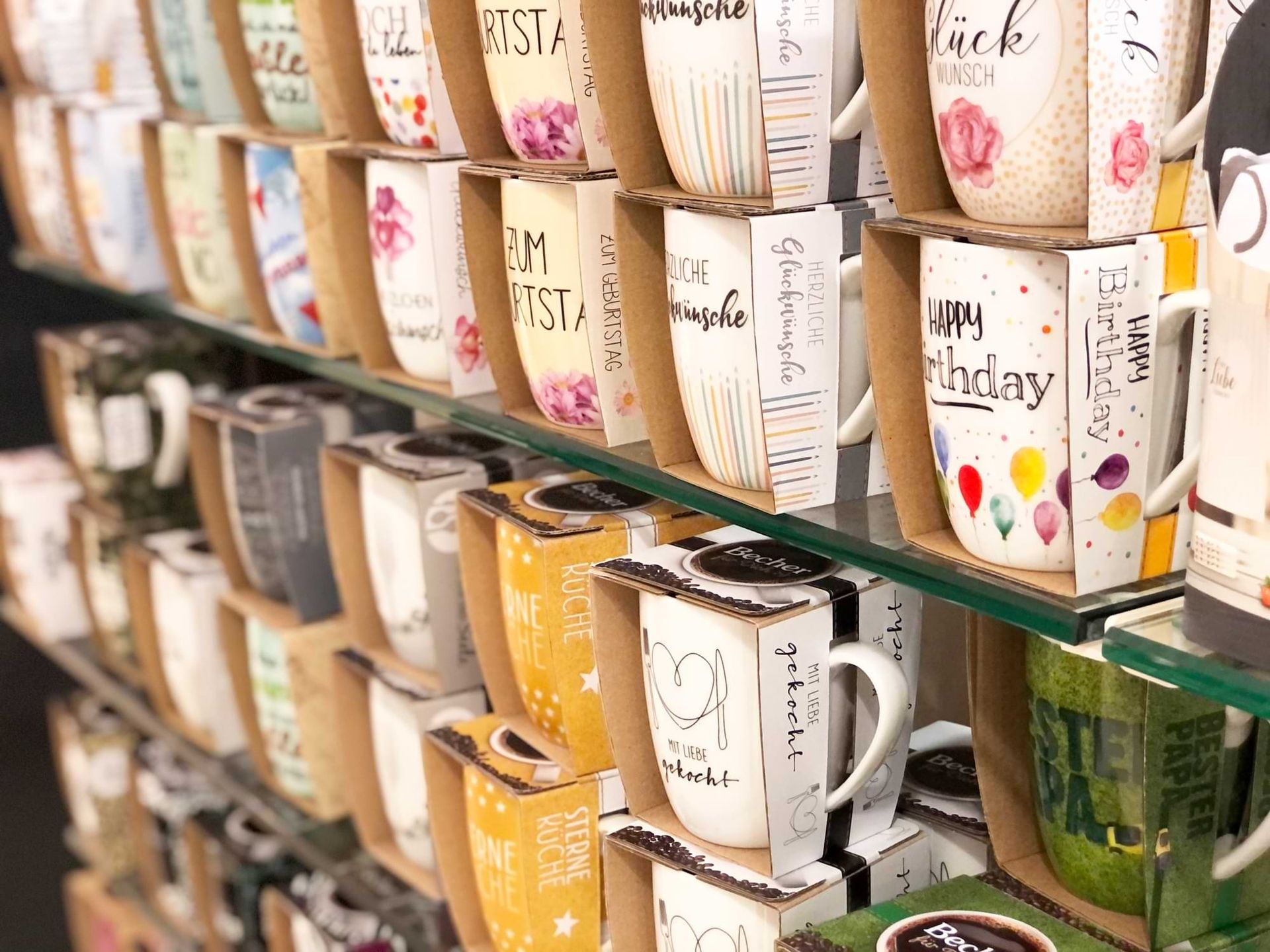 Eine Vielzahl von dekorativen Tassen mit farbenfrohen Motiven und Botschaften für Geburtstage und besondere Anlässe