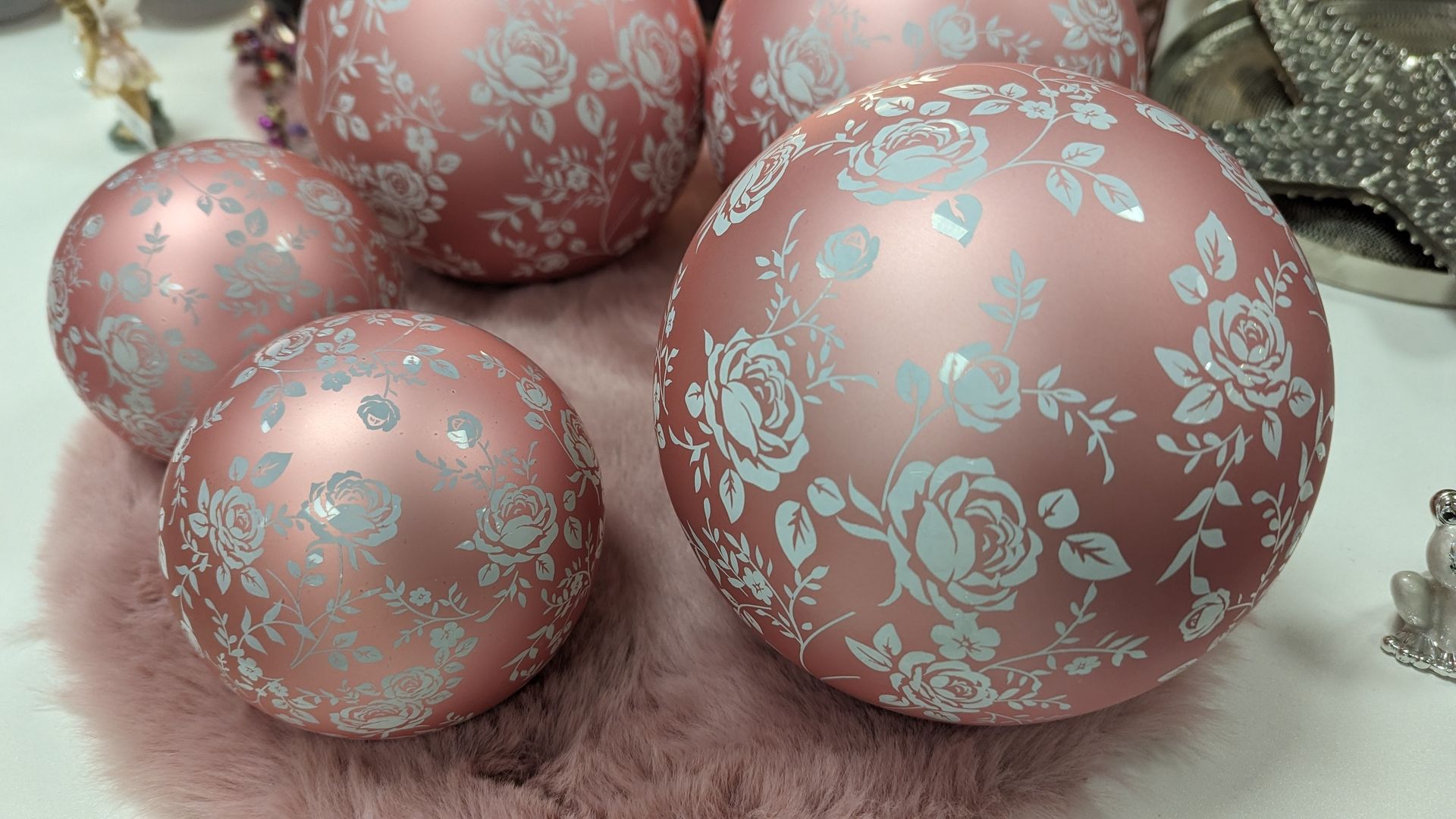 Eine Reihe von rosafarbenen Dekokugeln mit weißen Blumenmustern, die auf einer weichen, rosafarbenen Oberfläche angeordnet sind